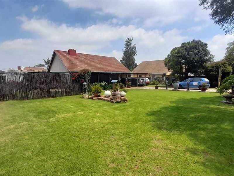 A spacious, well-maintained backyard garden featuring a large lawn, perimeter boundary walls, and views of the rear building elevations.