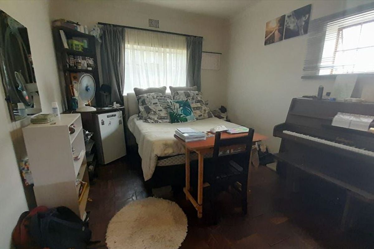 A bedroom featuring parquet flooring and a window with fitted blinds, offering a functional space with potential for modernization.