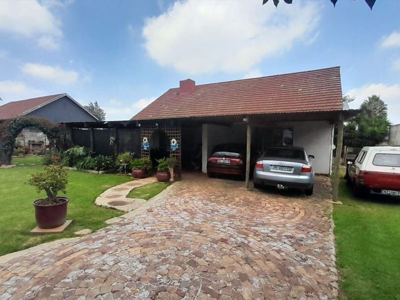 Front view of a residential property featuring a cobblestone driveway, a covered carport, and a well-maintained lawn area.