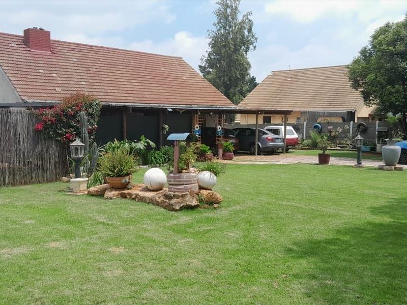 A spacious rear garden featuring a well-maintained lawn, a covered patio area, and a paved driveway leading to the main house structure.
