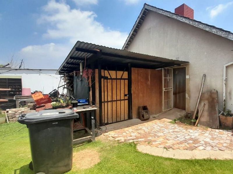 Rear view of the property showing a basic structure with a corrugated iron roof, brick paving, and a security gate entrance.