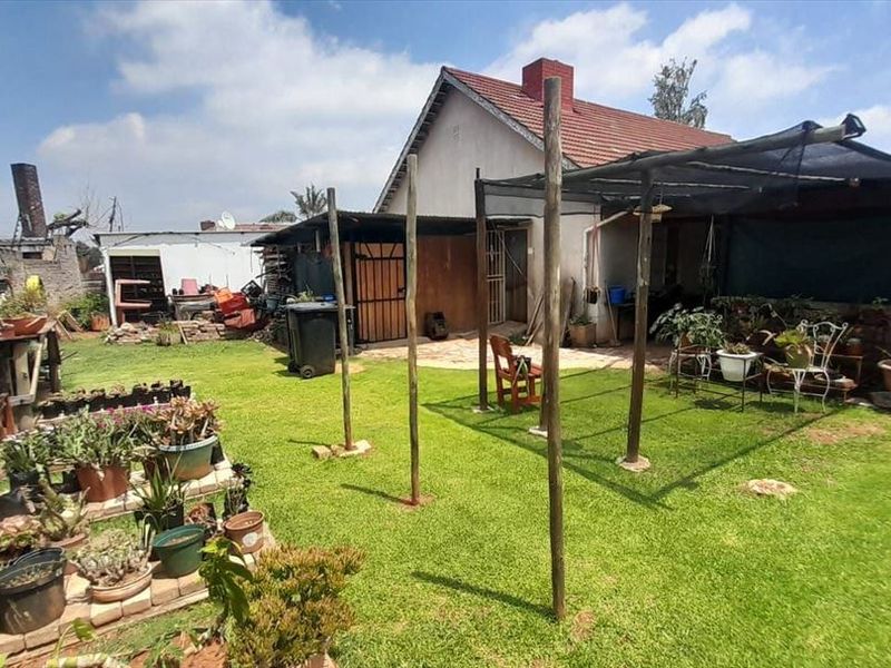 Rear garden area featuring a lawn, perimeter wall with electric fencing, and a basic covered patio structure attached to the main house.