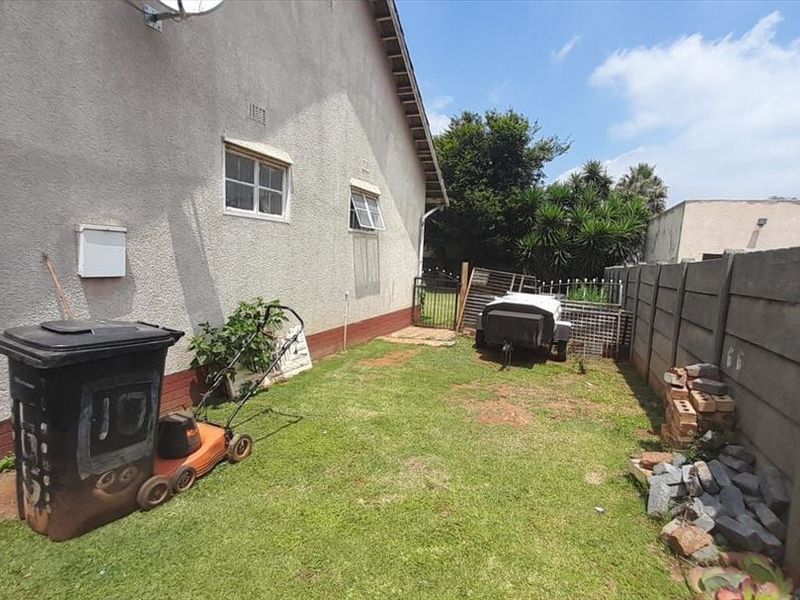 A side yard area featuring a lawn, precast concrete boundary wall, and metal gate access, showing signs of wear on the exterior wall base.