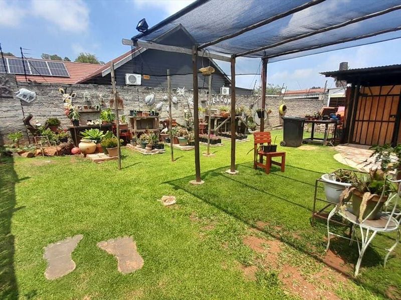 A private rear garden featuring a lawn, paved patio area, and a shade cloth structure, enclosed by a masonry boundary wall with solar panels visible.