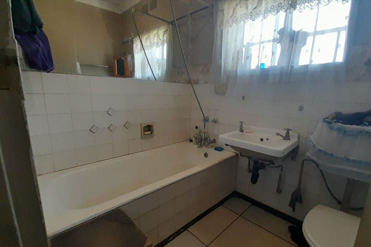 A dated bathroom featuring a standard bathtub, wall-mounted basin, and toilet with tiled finishes, offering potential for a modern renovation.