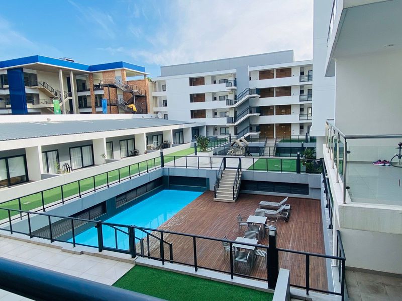 Communal pool area featuring a swimming pool, timber decking, and glass balustrades within a modern apartment complex.