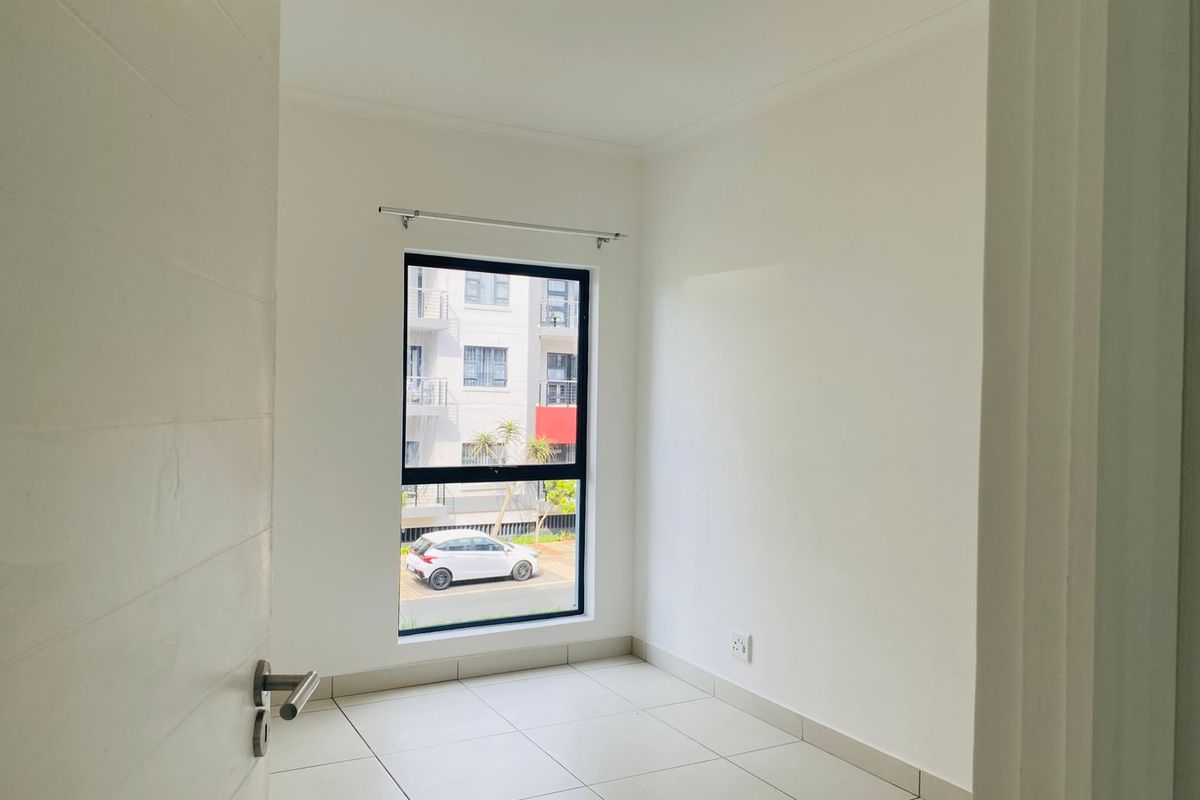 A bright, empty bedroom featuring neutral tiled flooring, a modern aluminium window frame, and clean white walls, ready for personalization.