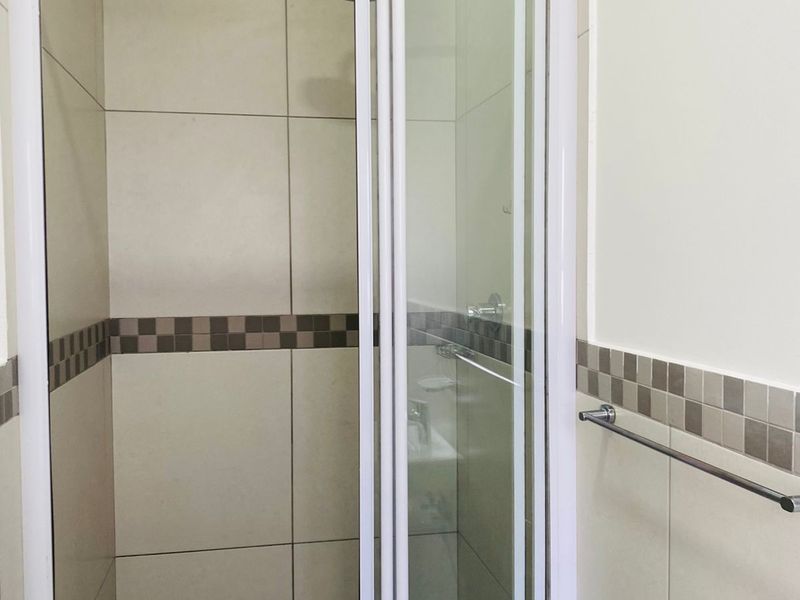 A clean, functional bathroom shower area featuring neutral wall tiles, a mosaic floor tile accent, and a modern shower head with a glass enclosure.