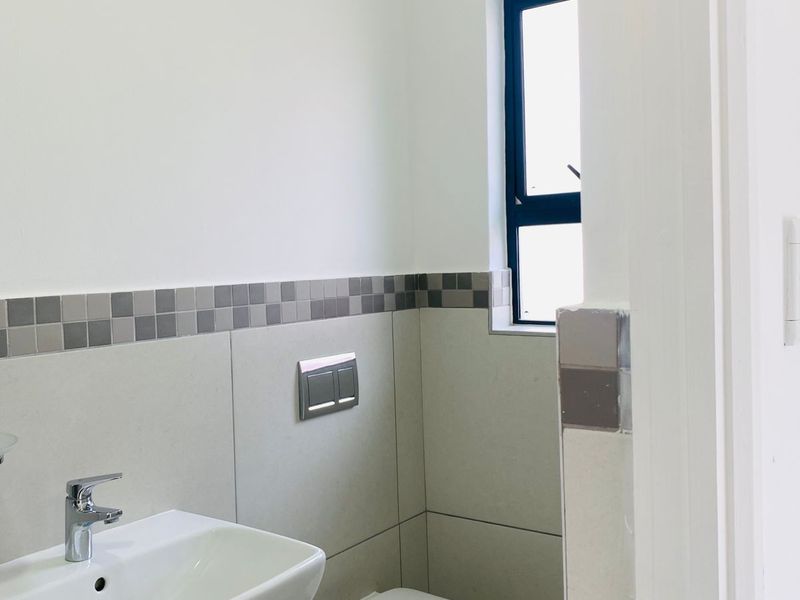 A modern, clean bathroom featuring a wall-mounted toilet with a concealed cistern, a wall-mounted basin, and neutral tiled finishes.