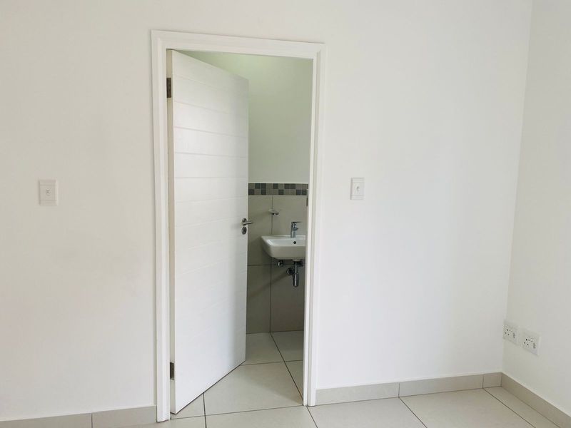 A view into a clean, minimalist bathroom featuring a wall-mounted basin with chrome fixtures and neutral floor tiling.