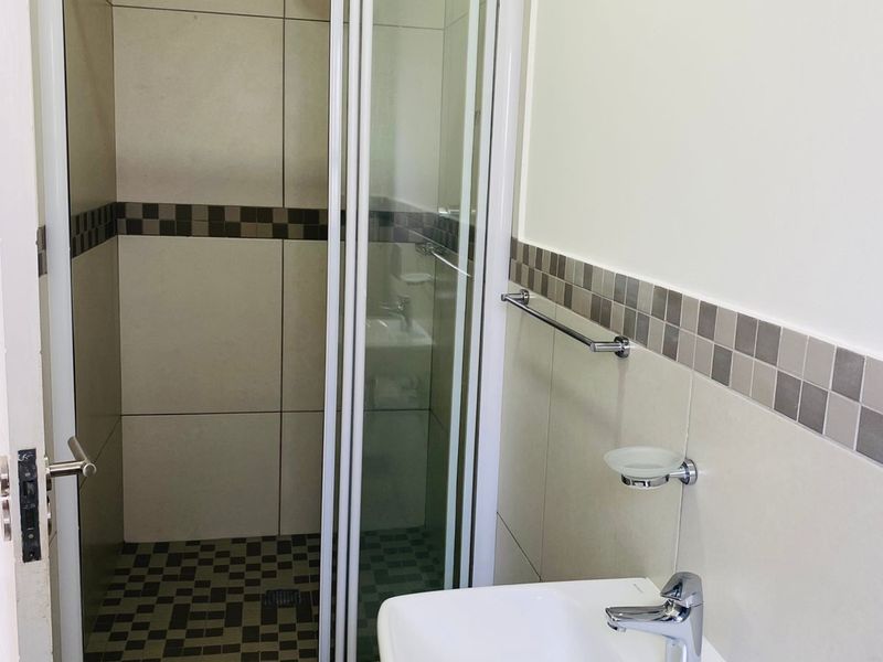 A clean, modern bathroom featuring a glass-enclosed shower, wall-mounted basin with chrome fixtures, and neutral tiled finishes.