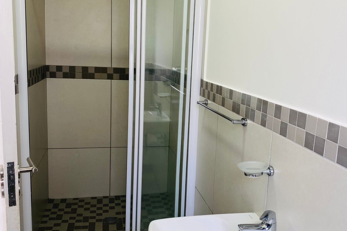 A clean, modern bathroom featuring a glass-enclosed shower, wall-mounted basin with chrome fixtures, and neutral tiled finishes.
