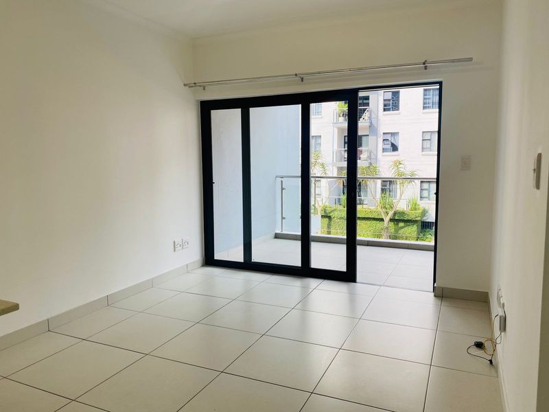 An empty, well-lit living area featuring neutral tiled flooring and a large sliding glass door that opens onto a private balcony.