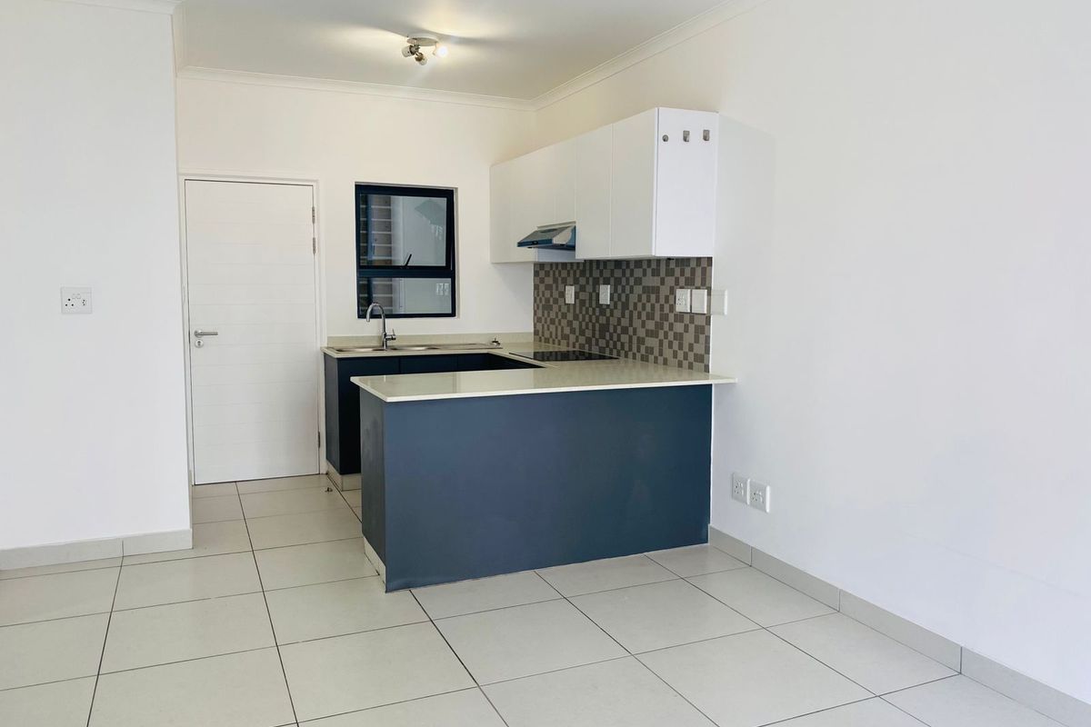 A clean, modern kitchen featuring dark base cabinets, white upper cabinetry, stone countertops, and a tiled splashback in an open-plan layout.
