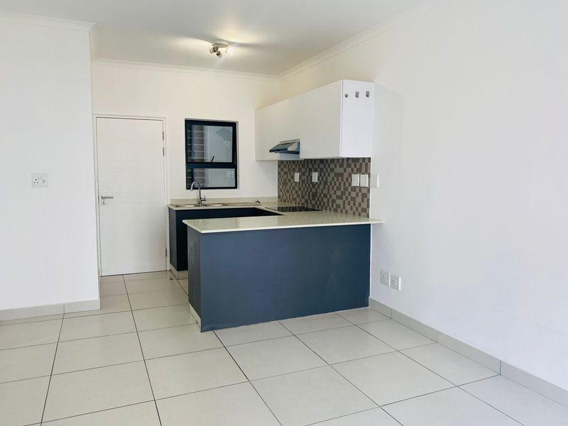 A clean, modern kitchen featuring dark base cabinets, white upper cabinetry, stone countertops, and a tiled splashback in an open-plan layout.