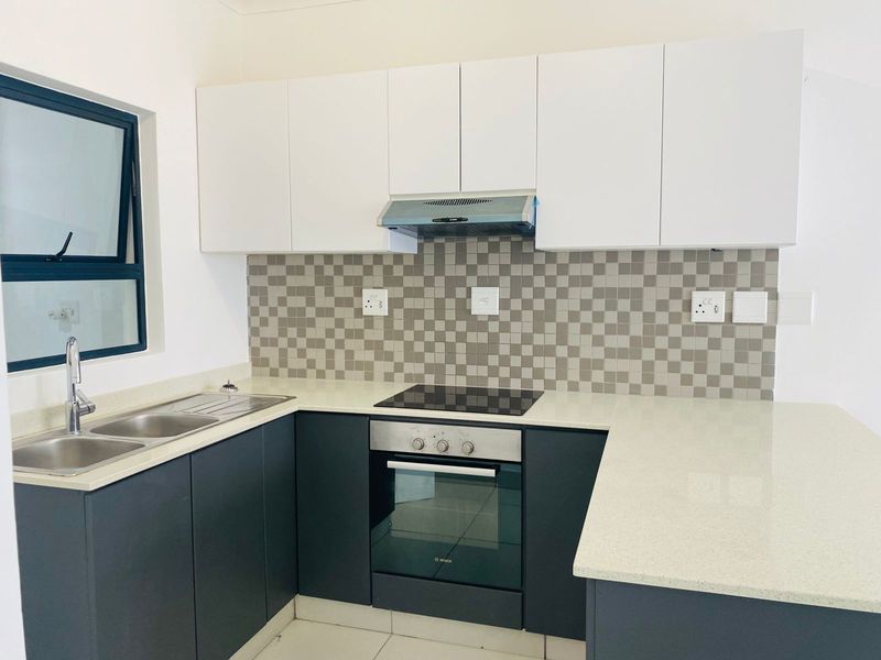 Modern kitchen featuring dark lower cabinetry, white upper cabinets, stone countertops, integrated oven, electric hob, and a tiled backsplash.