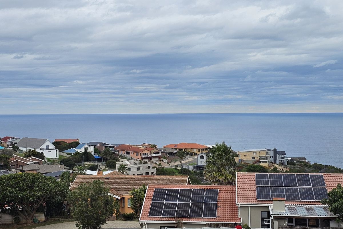 Elevated coastal view overlooking a residential neighborhood with visible solar panel installations on tiled roofs.
