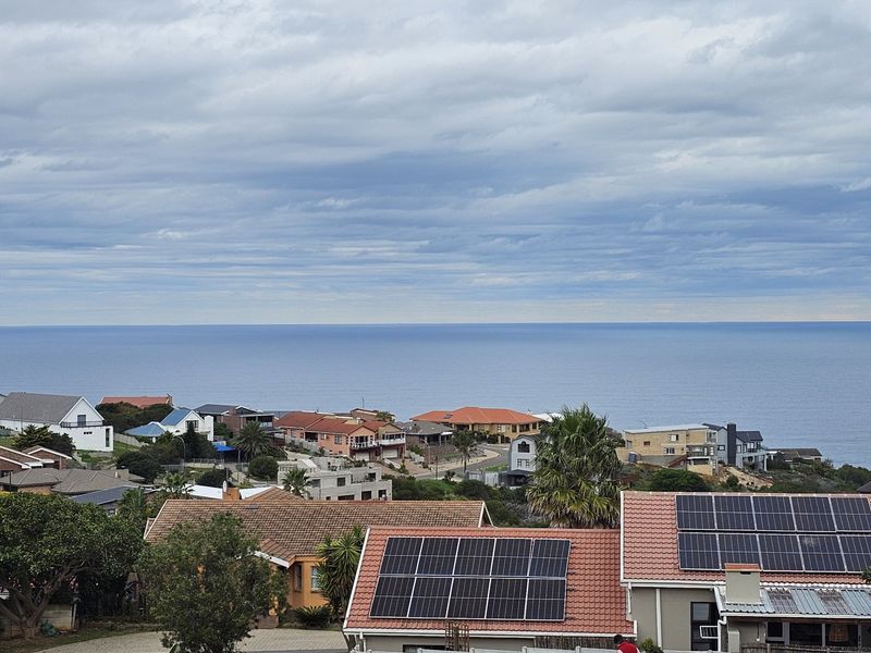 Elevated coastal view overlooking a residential neighborhood with visible solar panel installations on tiled roofs.