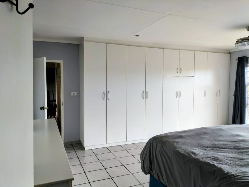 A bedroom featuring extensive white built-in cupboards, tiled flooring, and a ceiling fan, offering ample storage space.