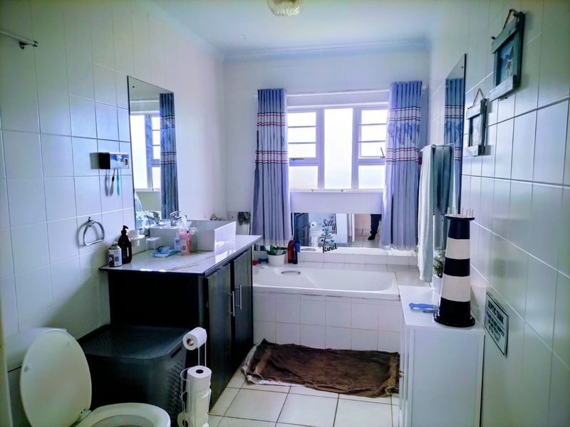 A functional bathroom featuring a built-in vanity with a vessel sink, a tiled bathtub surround, and full-height wall tiling.