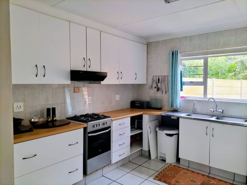 A functional kitchen featuring white cabinetry, a gas stove with extractor fan, double sink, and tiled backsplash with neutral floor tiles.
