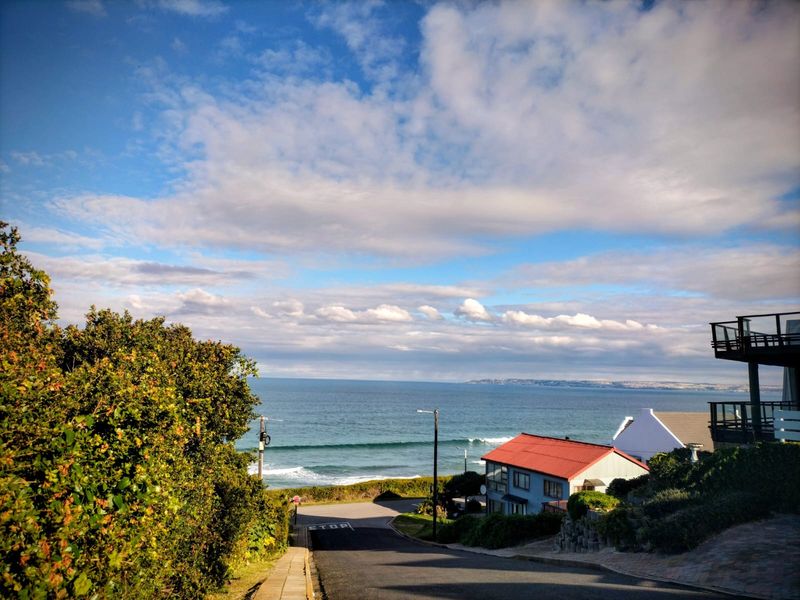 A scenic elevated view overlooking a coastal road leading towards the ocean with clear blue skies.