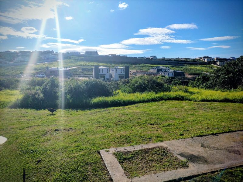 A view of the vacant residential land featuring natural grassland and a concrete foundation slab, with surrounding neighborhood development in the background.