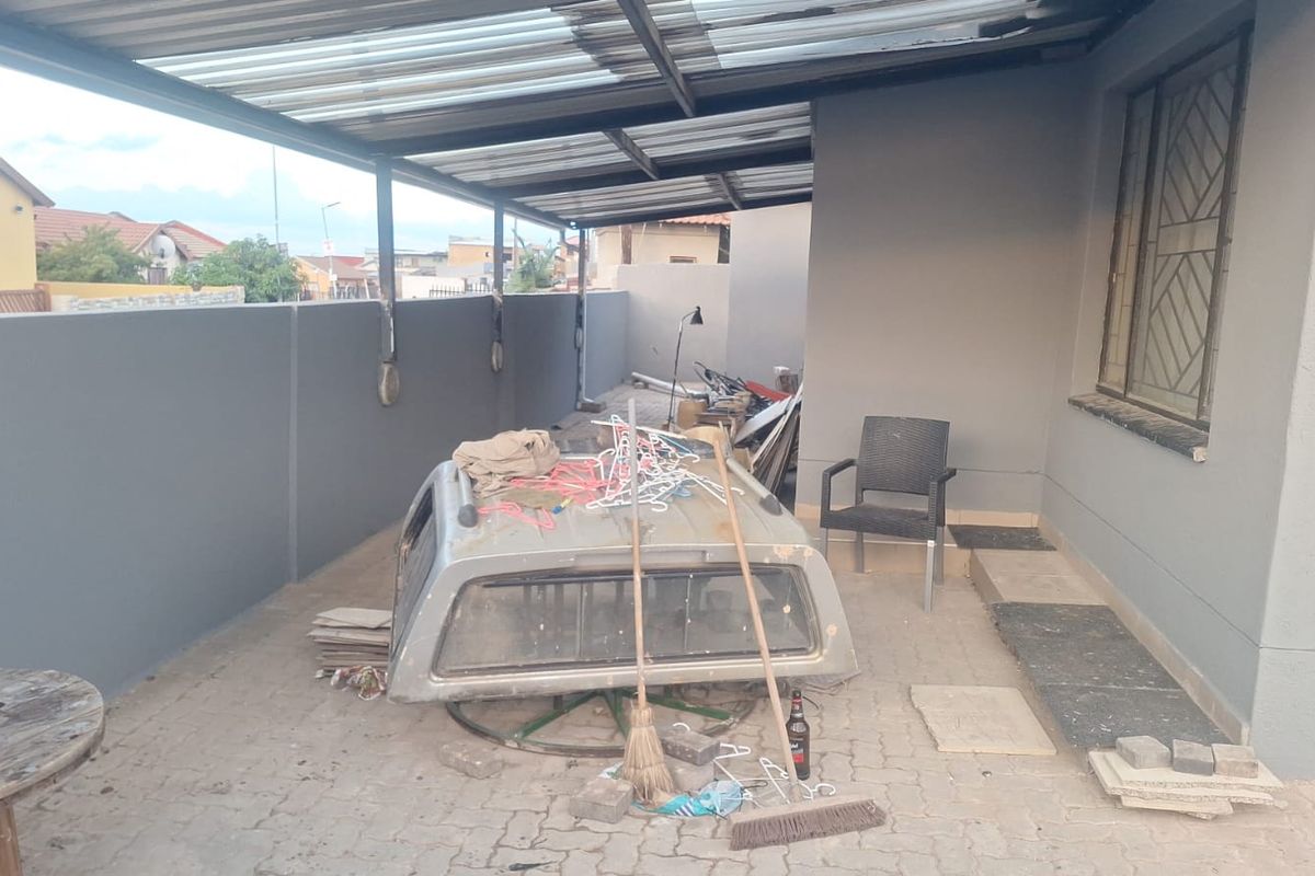 A covered outdoor patio area featuring paved flooring, a corrugated roof structure, and perimeter walling, providing a functional space for outdoor use.