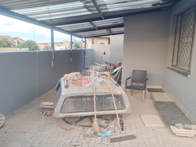 A covered outdoor patio area featuring paved flooring, a corrugated roof structure, and perimeter walling, providing a functional space for outdoor use.