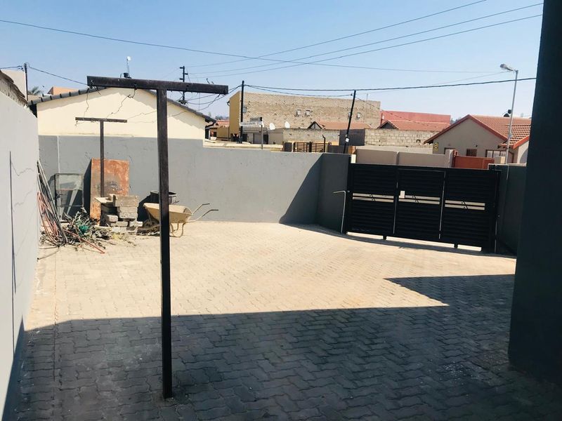 A paved front driveway area featuring a perimeter wall and a secure metal sliding gate, providing functional off-street parking space.