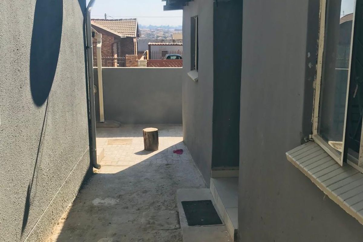 A narrow side passage or rear exterior area featuring a paved walkway, external wall lighting, and a satellite dish mounted on the wall.