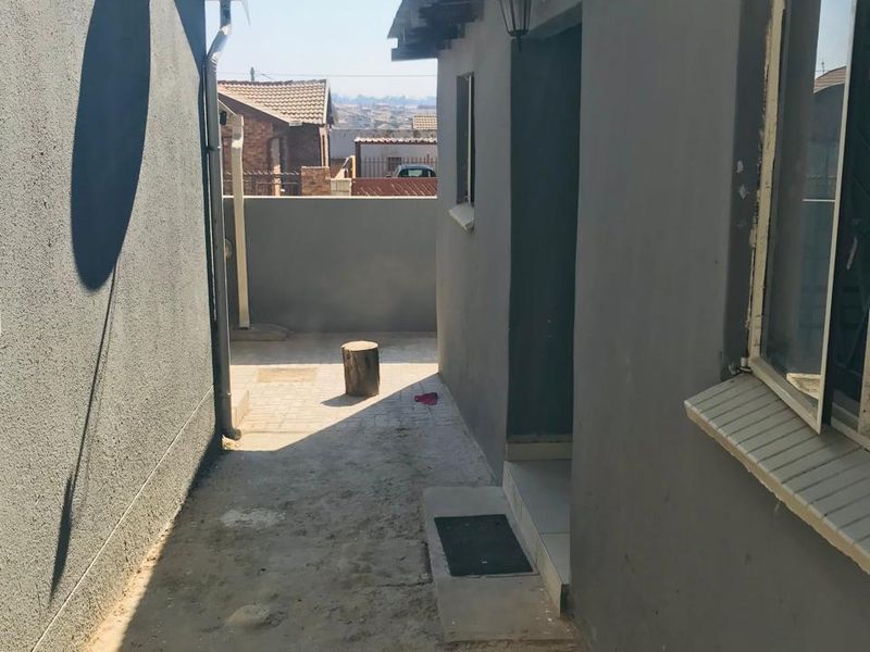 A narrow side passage or rear exterior area featuring a paved walkway, external wall lighting, and a satellite dish mounted on the wall.