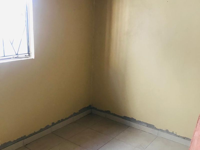 An empty bedroom featuring tiled flooring, security bars on the window, and exposed timber roof rafters, currently in need of finishing and cosmetic updates.