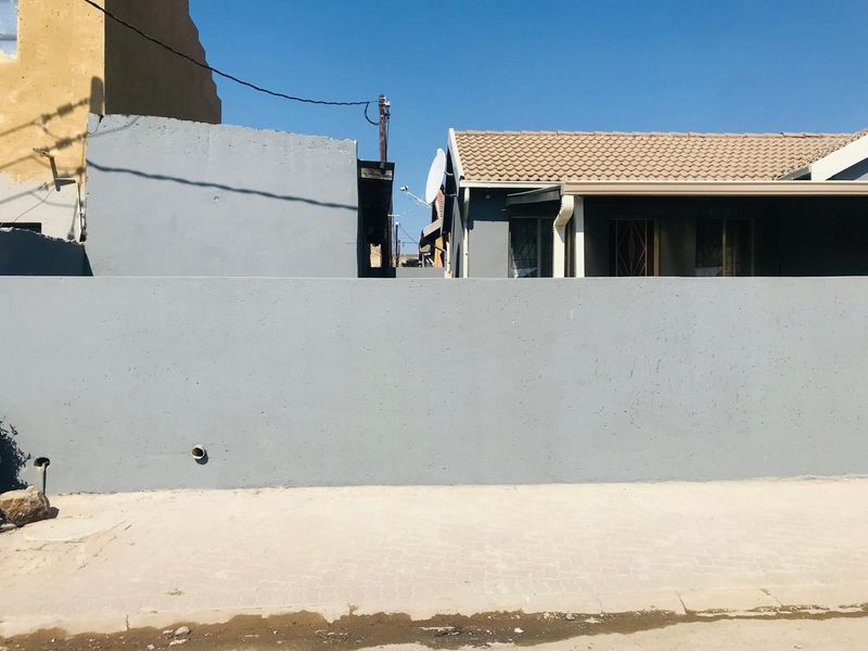 A street-level view of the property featuring a solid boundary wall, tiled roof, and security gates on the windows.