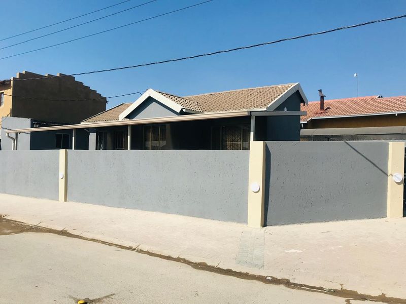 Front exterior view of a house featuring a grey perimeter wall, tiled roof, and paved driveway area.