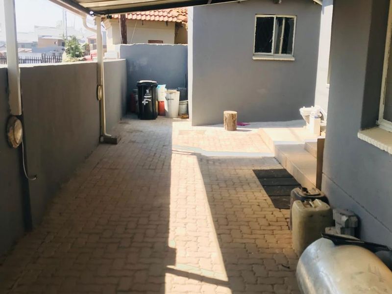 A covered outdoor patio area featuring paved flooring and a corrugated metal roof, providing a functional utility space.