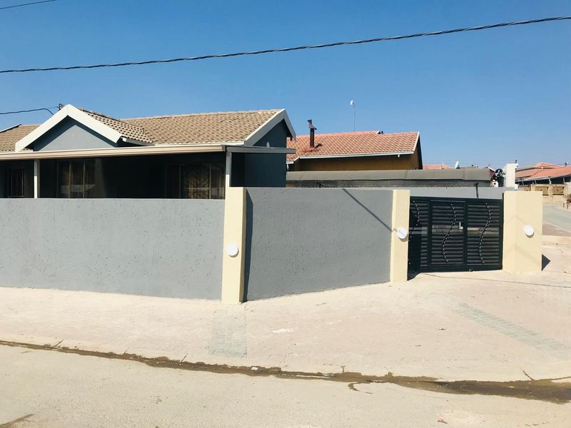 Front view of the property featuring a modern grey perimeter wall, secure metal driveway gate, and a tiled roof structure.