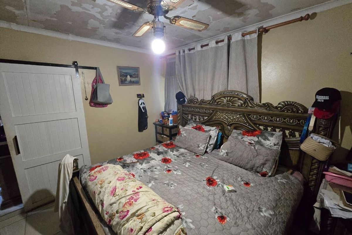 A bedroom featuring a ceiling fan, tiled flooring, and a sliding barn door, currently showing significant signs of ceiling paint deterioration and water damage.