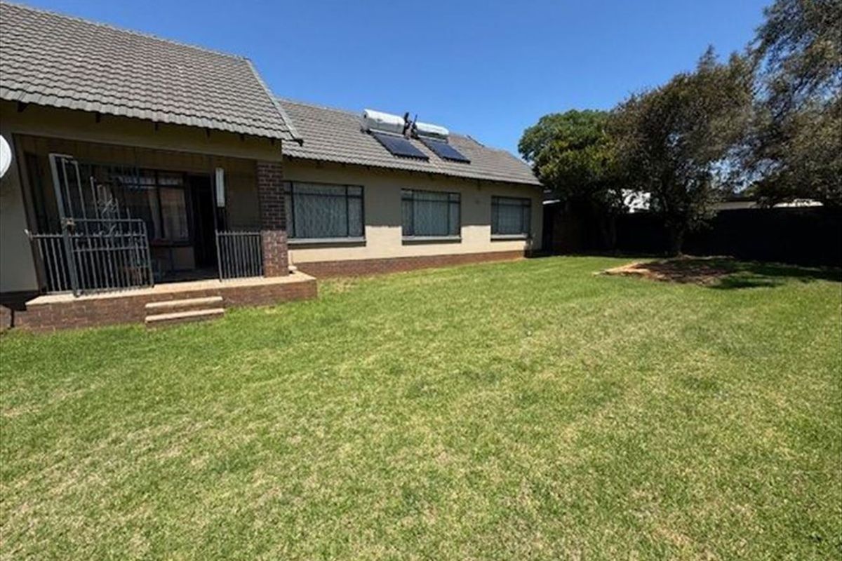 Rear view of the house featuring a spacious lawn, covered patio area, and roof-mounted solar water heating panels.