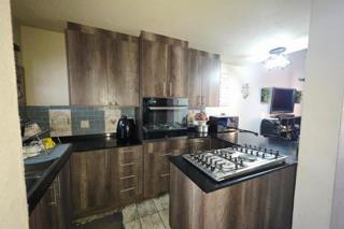 Modern kitchen featuring wood-finish cabinetry, granite countertops, a built-in oven, and a gas hob on a central island.