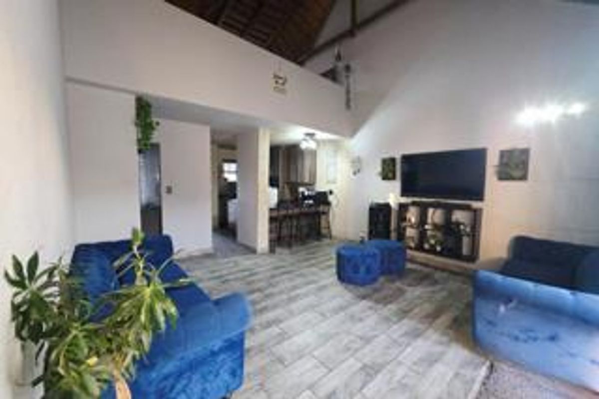 Open plan living area featuring high vaulted ceilings with exposed rafters, tiled flooring, and a connected kitchen space with a breakfast bar.