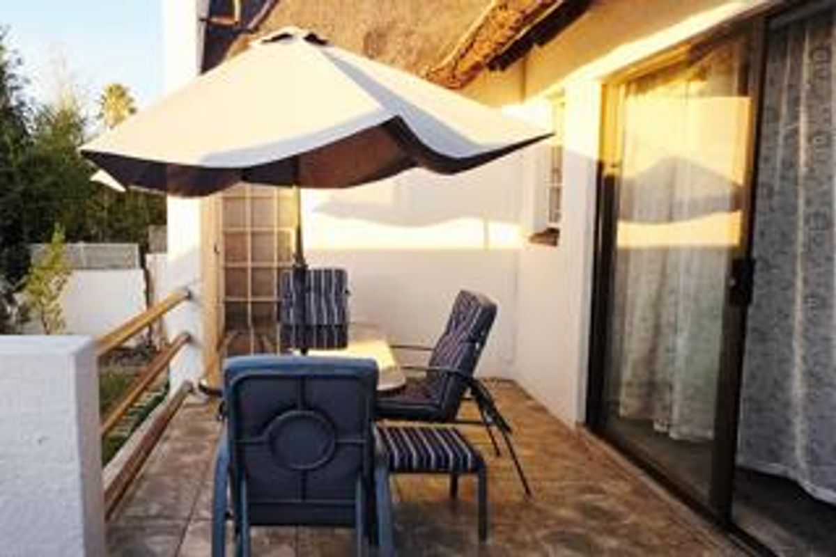 A covered patio area featuring tiled flooring, a sliding glass door entrance, and a thatched roof overhang, providing a functional outdoor living space.