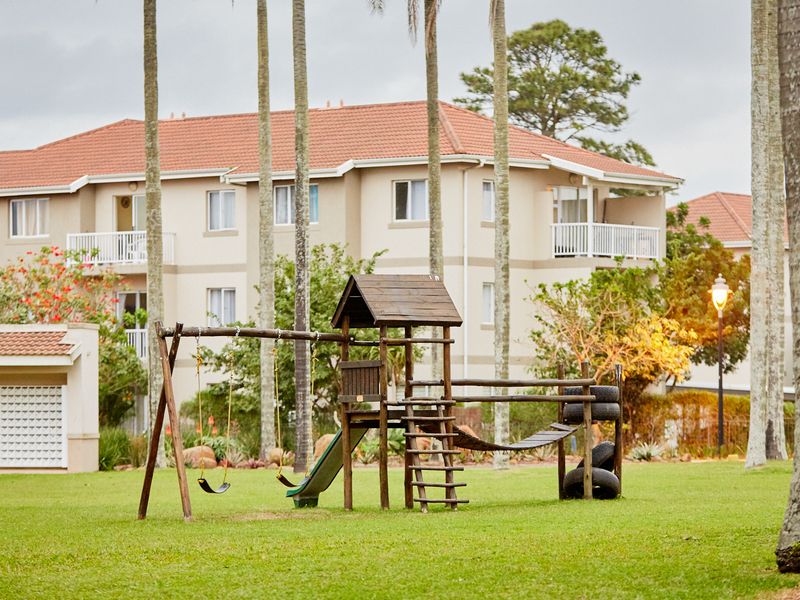 A well-maintained communal garden area featuring a children's playground set, surrounded by apartment building facades and mature trees.