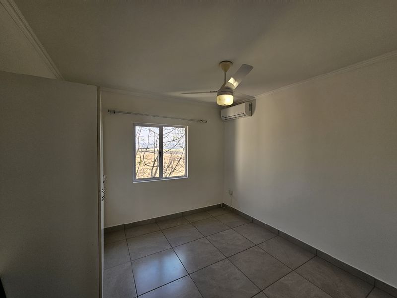 A clean, empty bedroom featuring tiled flooring, a ceiling fan, a split-system air conditioner, and a built-in wardrobe.