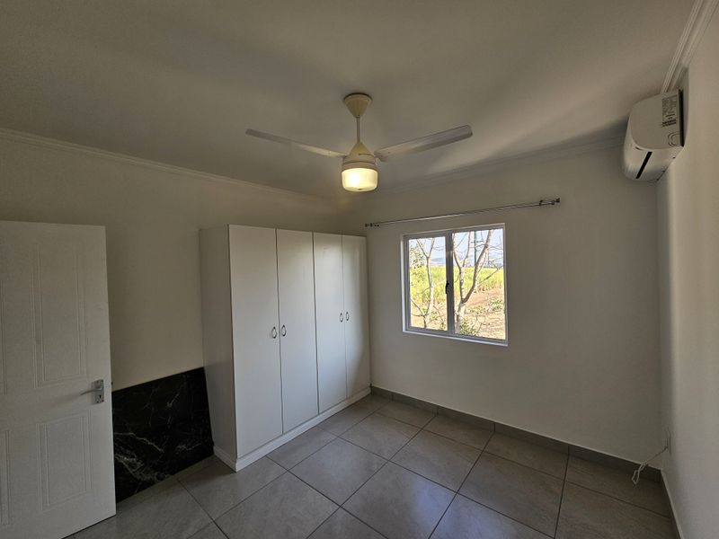 A clean, empty bedroom featuring tiled flooring, a built-in wardrobe, a ceiling fan, and a wall-mounted air conditioning unit.