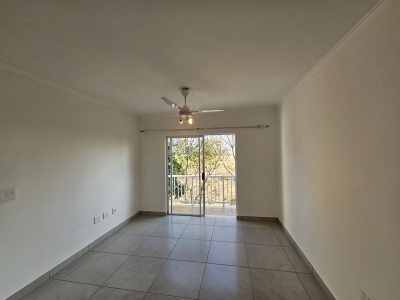 An empty living room featuring neutral tiled flooring, a ceiling fan, and a sliding glass door providing access to an outdoor balcony.