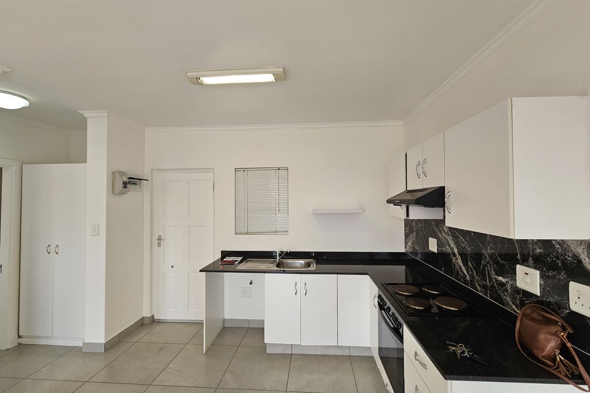 A clean, functional kitchen featuring white cabinetry, black granite countertops, marble-effect splashbacks, and integrated appliances, including an electric hob and oven.