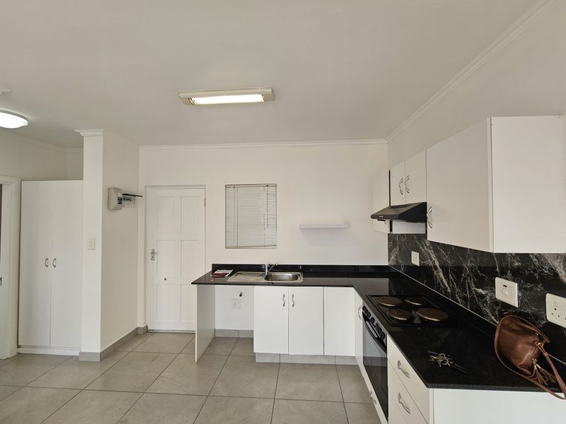 A clean, functional kitchen featuring white cabinetry, black granite countertops, marble-effect splashbacks, and integrated appliances, including an electric hob and oven.