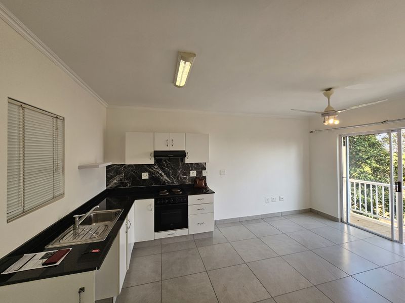 Open-plan kitchen and living area featuring modern cabinetry, black granite countertops, tiled flooring, and direct access to a private balcony through sliding glass doors.