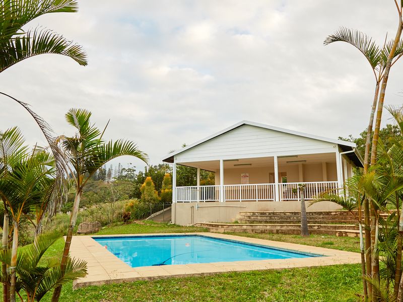 A well-maintained outdoor pool area featuring a rectangular swimming pool and a covered patio with white railings, set within a landscaped garden.
